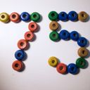 On a white surface, multicolour painted wooden beads aligned in the forms of the digits seven and five.