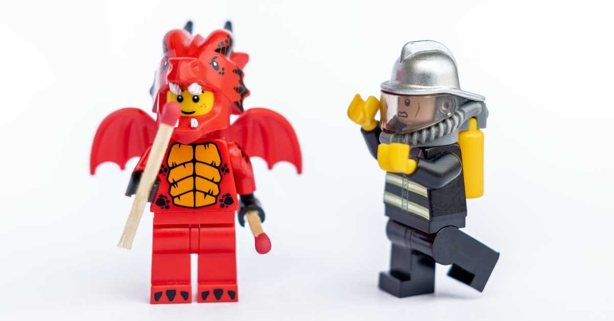 Zwei Lego-Figuren, eine davon ist ein kleiner Teufel mit einem Streichholz in der Hand, die andere ein Feuerwehrmann.