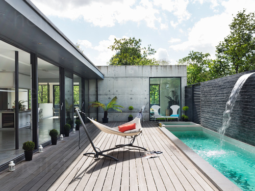 Outdoor deck next to stylish architectural home with prominent water feature and large free standing hammock Zoom background