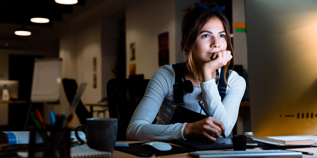 Best Free UX Training Online An aspiring UX writer sitting at a desk with a lamp, taking notes in front of a screen.