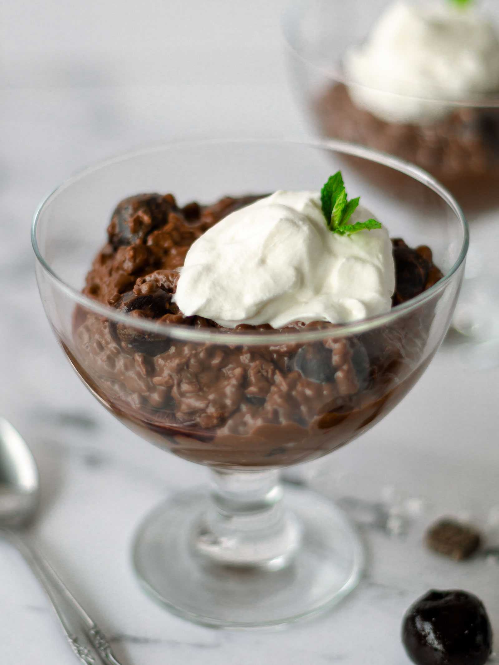 Image of a serving of Chocolate Cherry Chia Puddling in a glass cup, with a dollop of whip cream on top. This is a healthy dessert or breakfast on the go. This delicious combination of chia seeds, cherries, and dark chocolate is not only healthy but quite decadent.