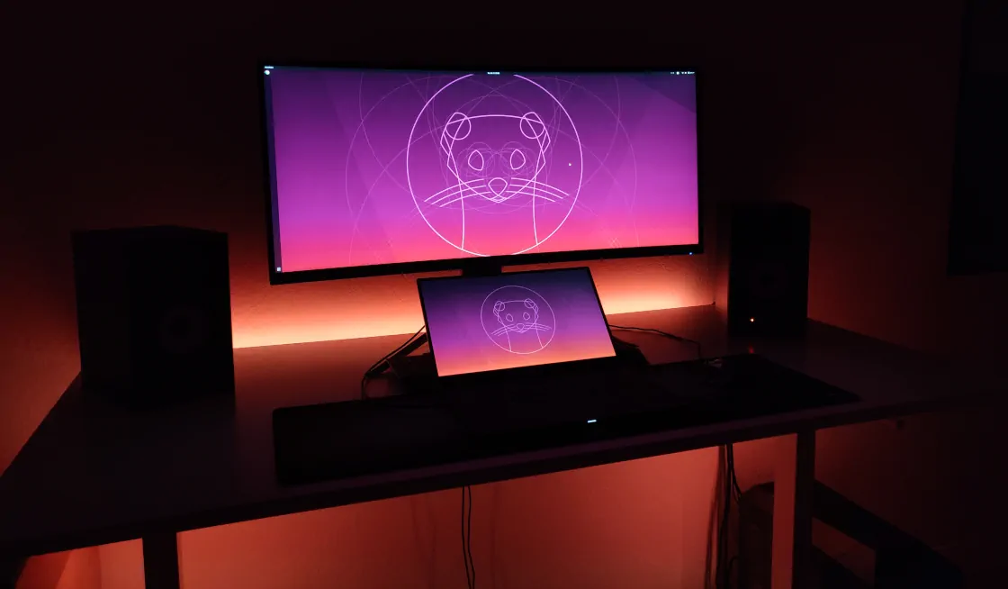 Orange illuminated desk with ultra-wide monitor and notebook showing the Ubuntu 19.10 “Eoan Ermine” wallpaper.