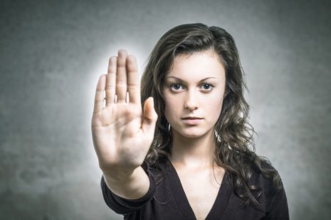 Eine Frau mit ausgestrecktem Arm, Handflächen noch vorne und selbstbewusstem Gesichtsausdruck.