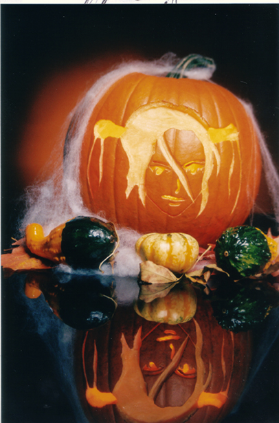 A pumpkin with a carving of an anime character sits on top of a glass surface.