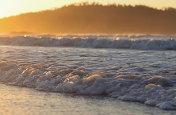 Destaque no mar com espumas de ondas e por do sol alaranjado refletindo na água