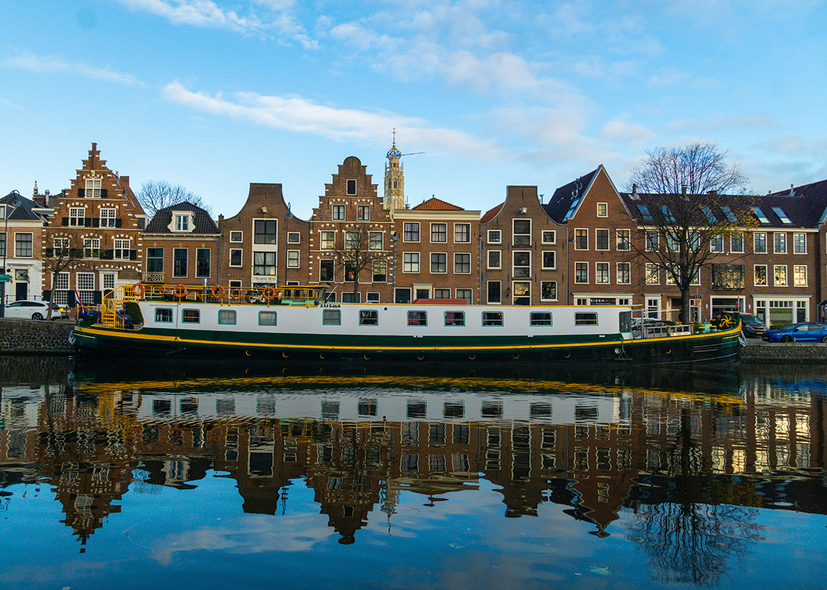 brown buildings along the water's edge with a boat on the canal in Haarlem, Netherlands