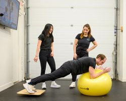 Two Integral therapists supervising a patient balancing on an exercise ball