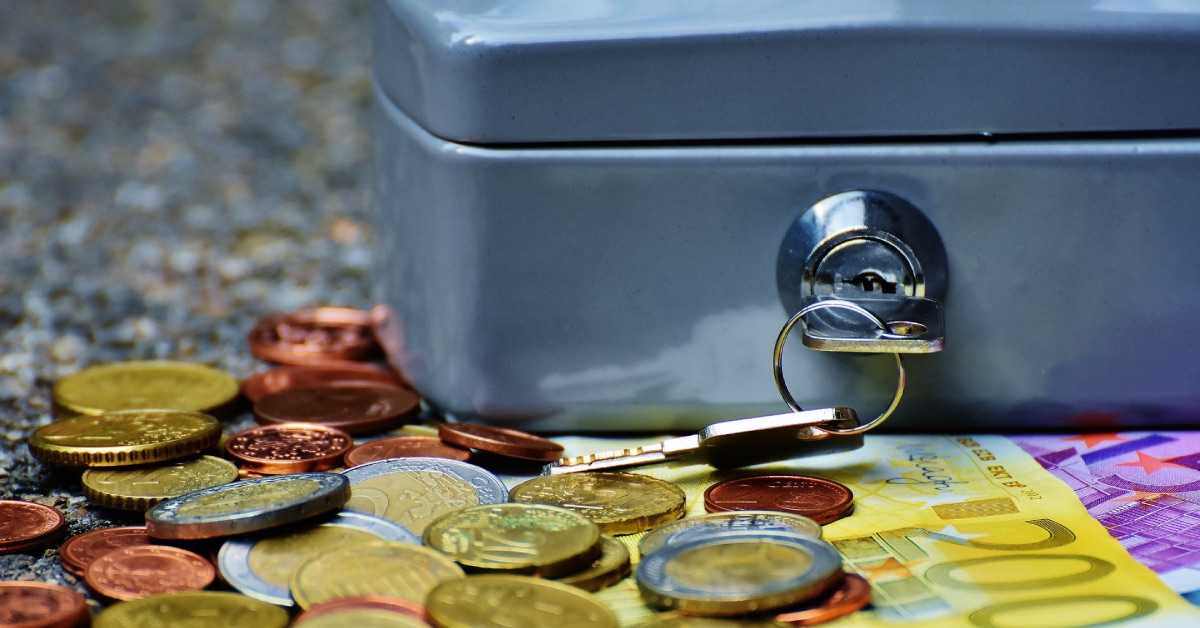Nahaufnahme einer verschlossenen Vereinskasse, davor liegen Münzen und Euro-Banknoten