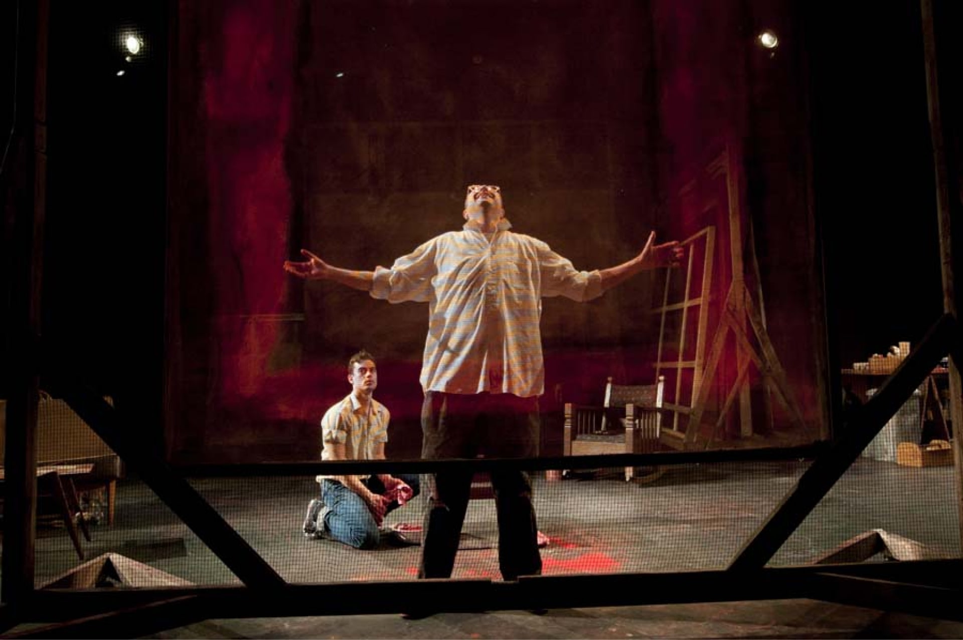 Man stands with arms outstretched seen through transparent canvas, with kneeling man in background.