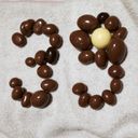 Two awkward digits, three and nine, formed with an arrangement of chocolate covered nibbles placed on a towel. The counter of the nine is a white “chocolate”.