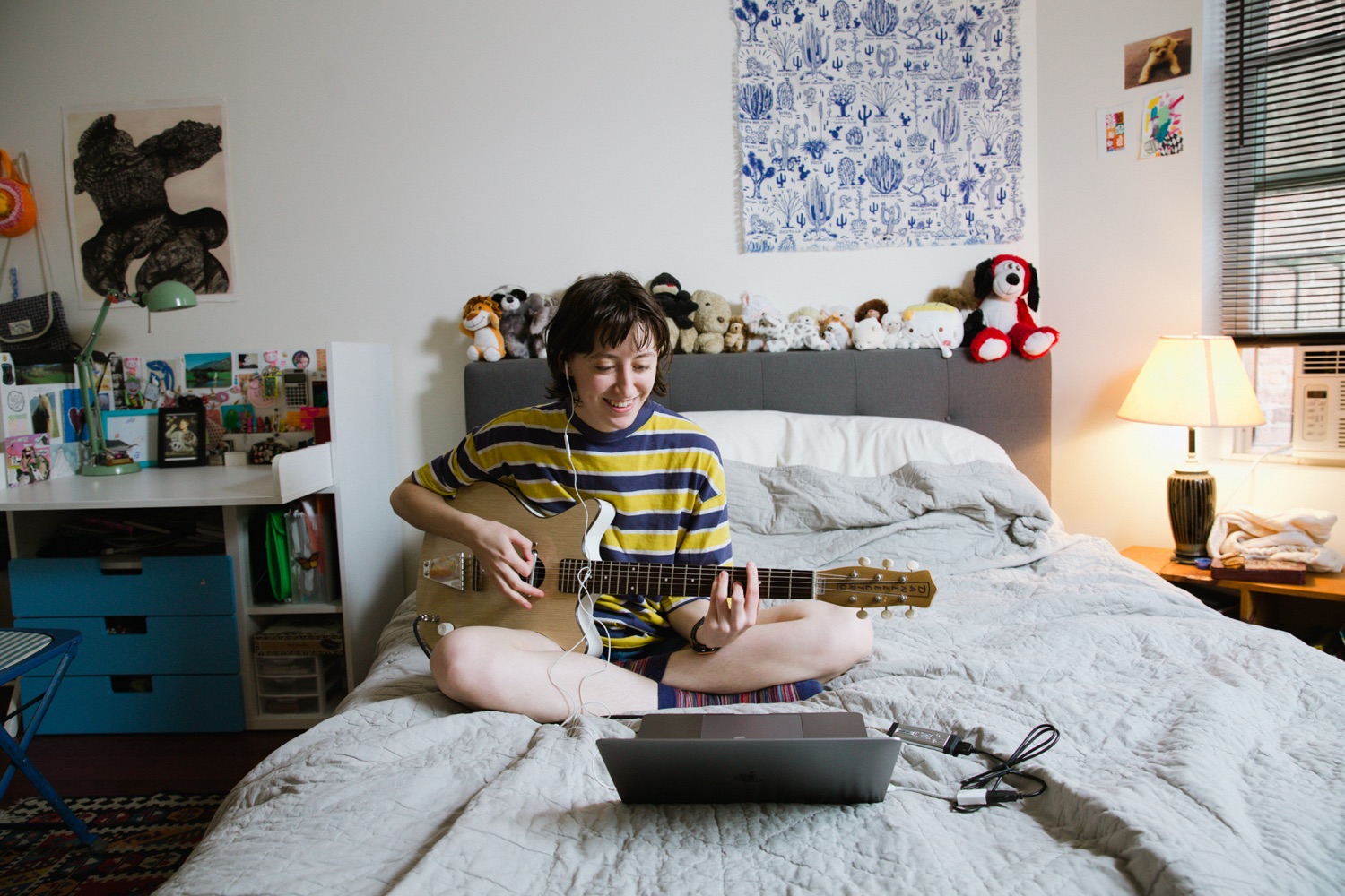 Greta Klein plays guitar on a bed