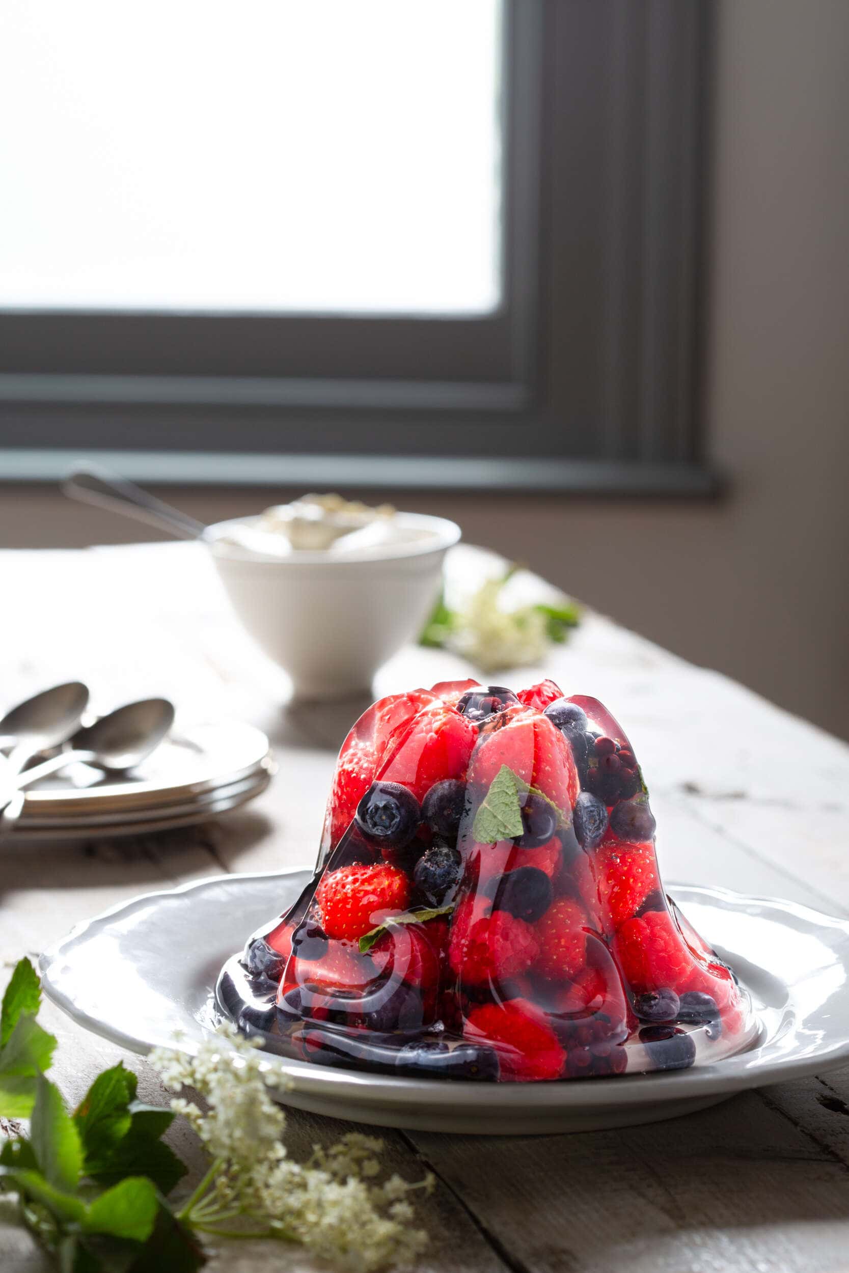 Elderflower and Prosecco fruit jelly set on a plate with elderflowers in the foreground and a window in the background.