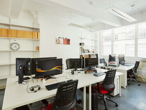 Modern shared workspace containing white computer desks with black office chairs in front of large windows Skype background