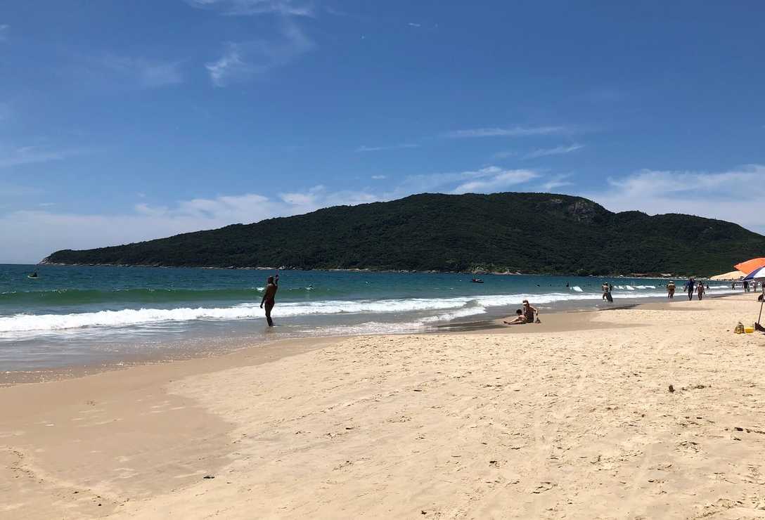 Vista da areia da praia dos Ingleses com céu azul ao fundo, guarda-sóis e pessoas