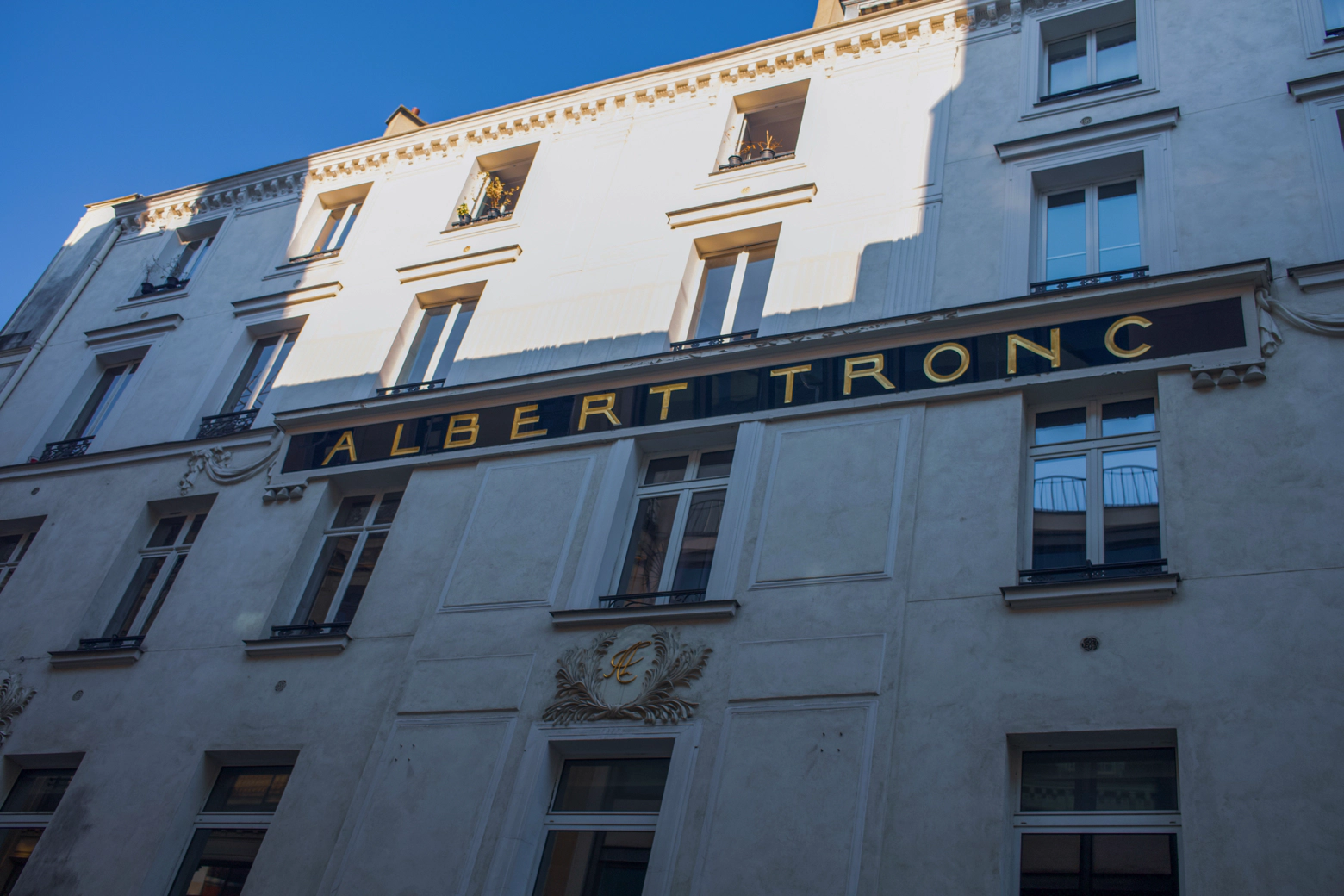 A large golden sign on a white building reads: 'Albert Tronc'