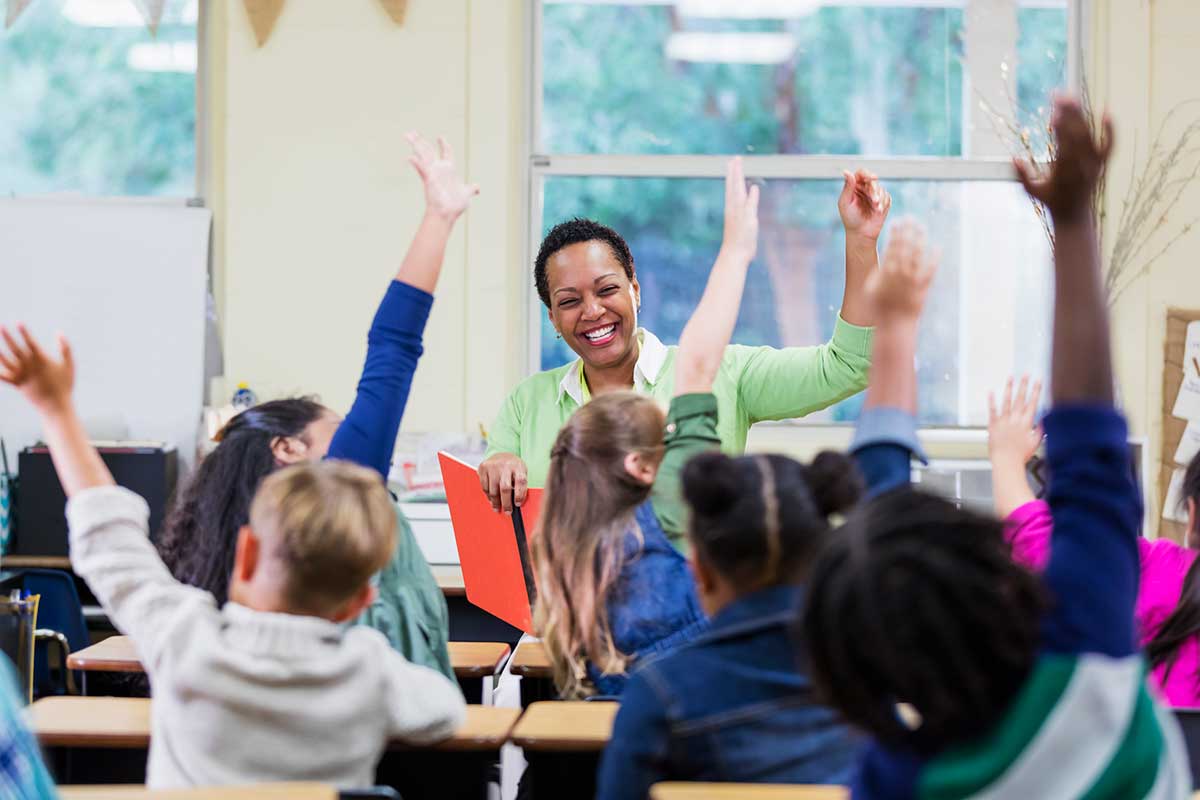 Friendly teacher smiles as her enthusiastic class raises their hands