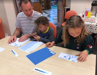 Man and two children at a table adding stickers to a sheet.