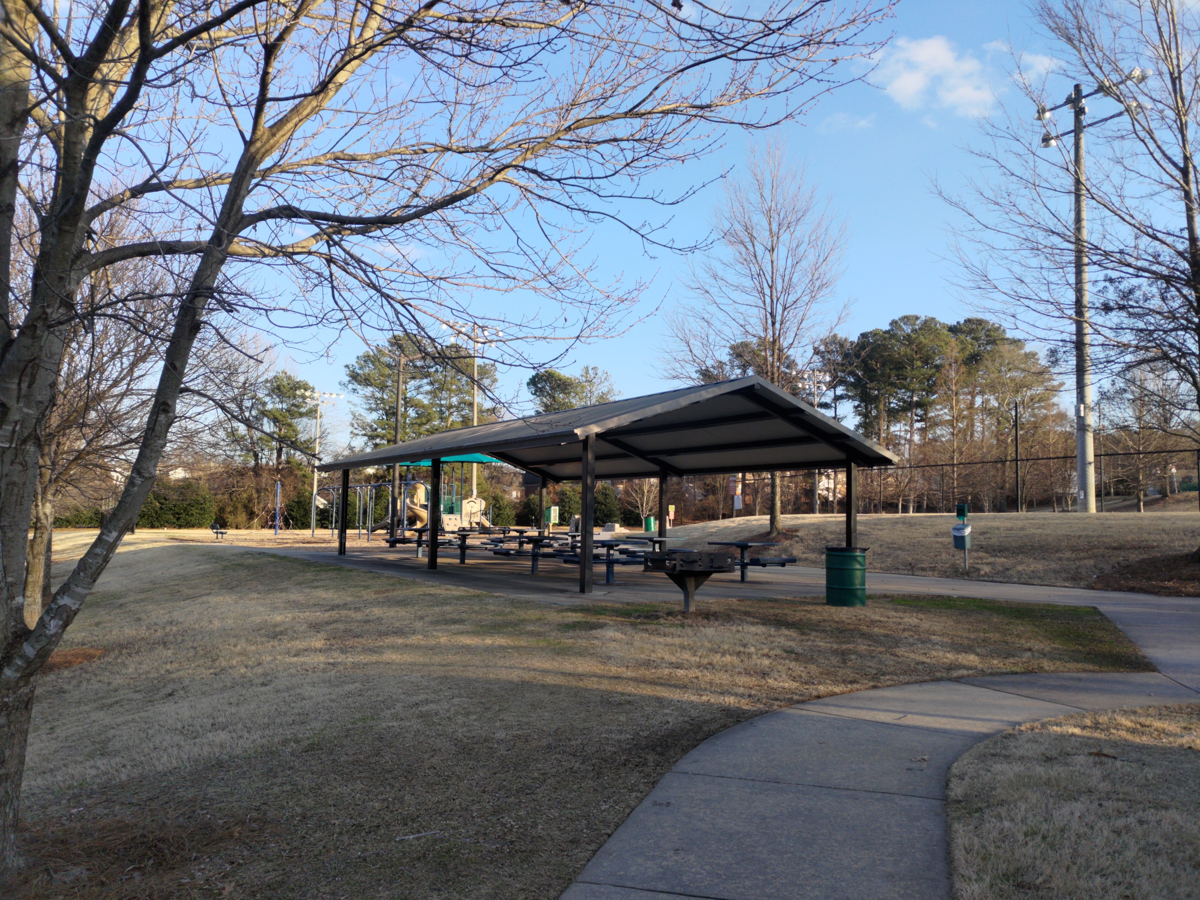 A pavilion and grilling area with a playground and field lighting in the background