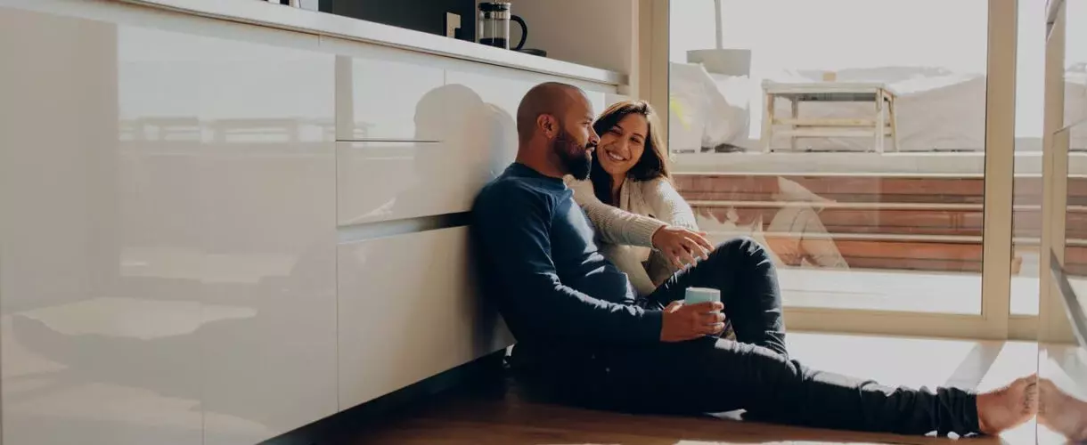 Smiling man and woman sitting on kitchen floor against cabinets