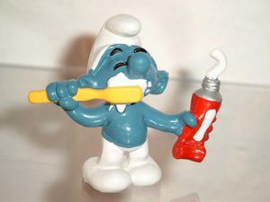 A Smurf figurine sitting on a table holding a toothbrush