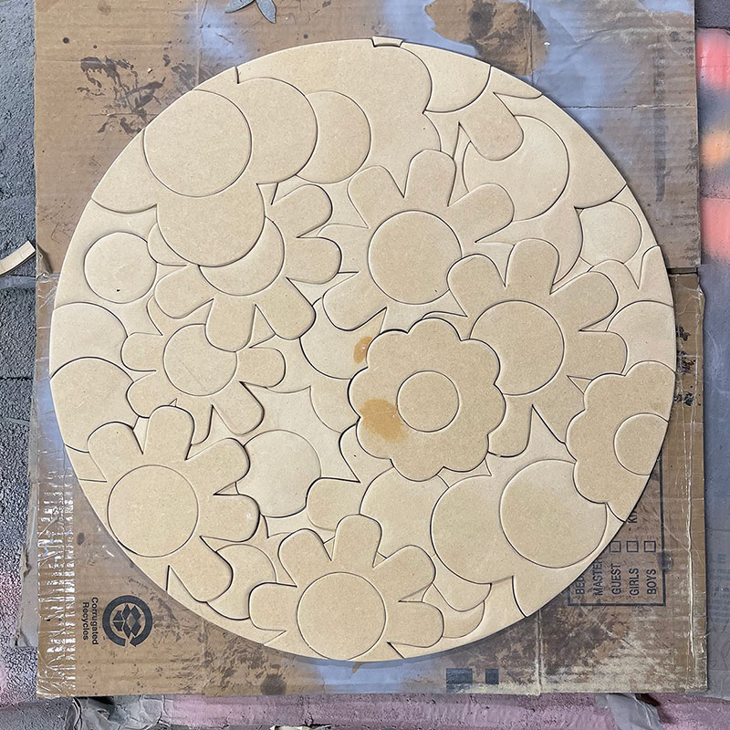 round wooden sign with cut outs in the shape of flowers on top of a piece of cardboard
