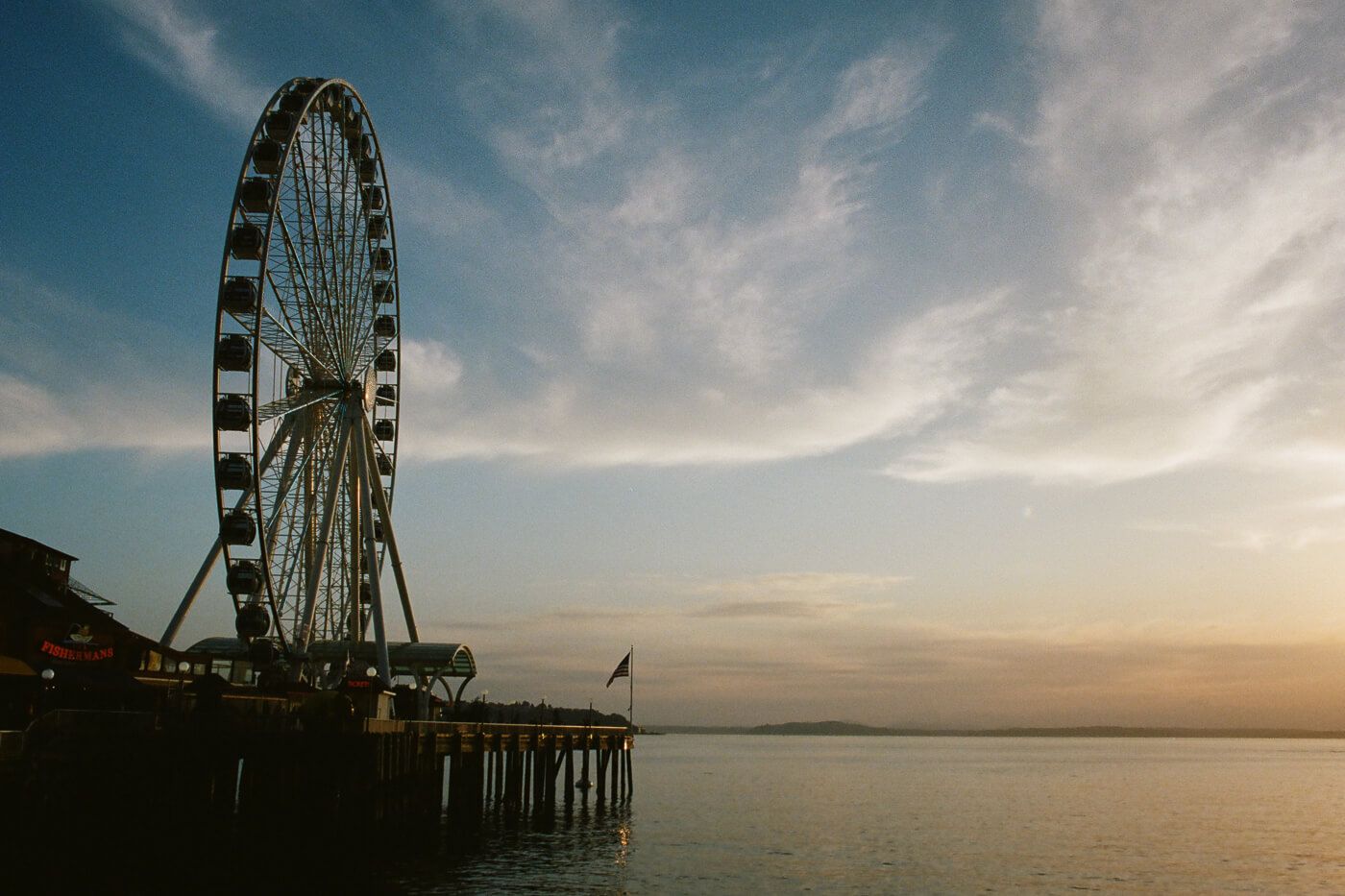 Ferris wheel on the pier beside the water, viewed from a distance