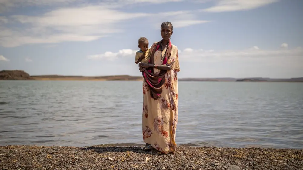 Woman standing at Lake Turkana holding a small child