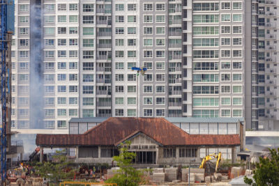 Matilda House, a single-storey colonial bungalow with a red roof and a black-and-white façade, stands amidst a construction site. A row of HDB flats stand behind it in the background.