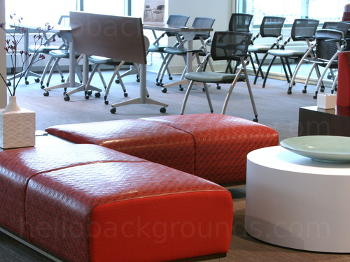 Sophisticated shared work space featuring corner red padded seating unit in front of multiple metal framed black chairs   Skype background