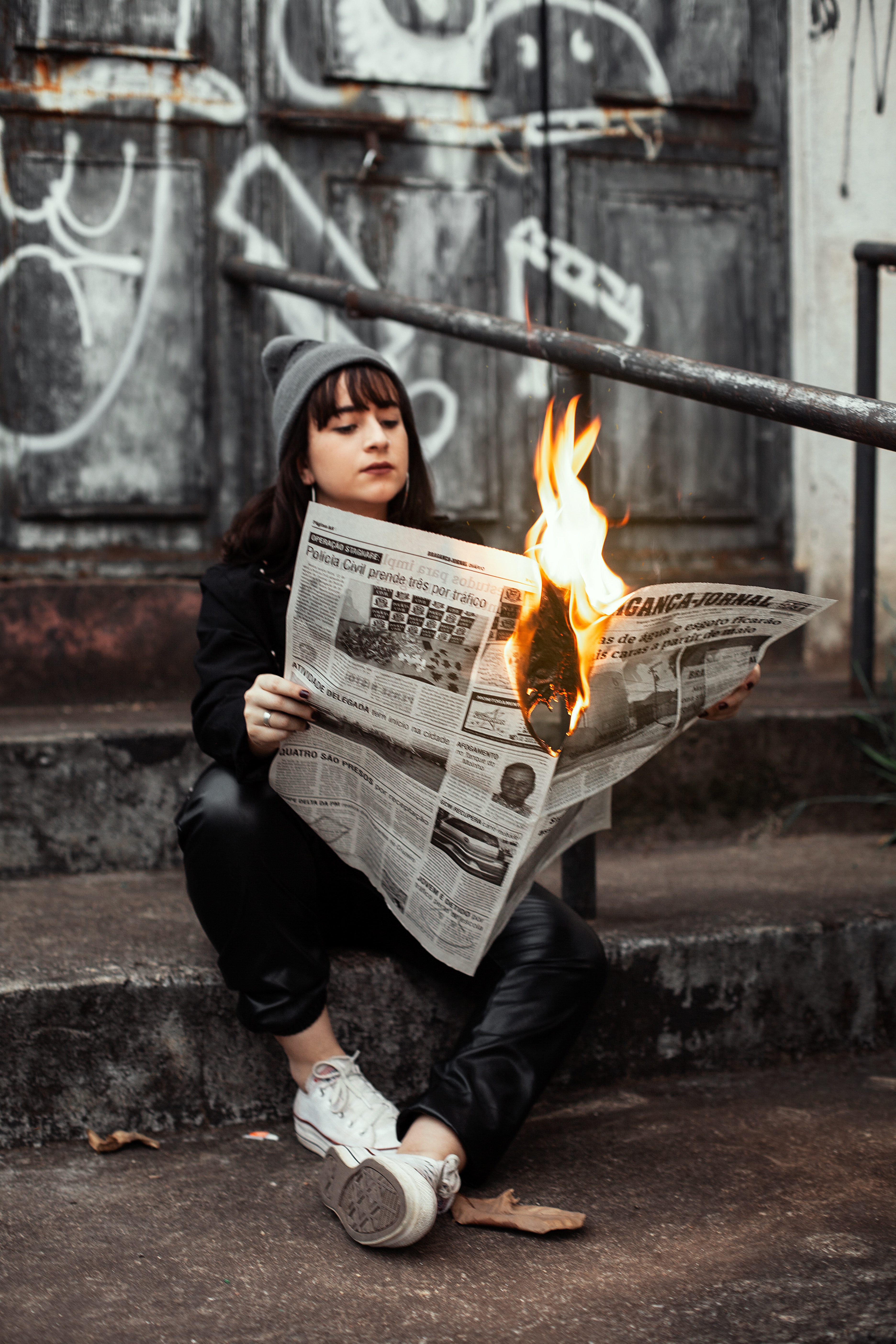 A woman sitting in an alleyway holding a burning newspaper  