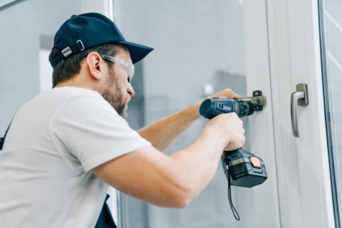 handyman in goggles fixing window handle by electric drill