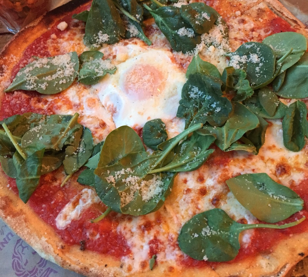a pizza with an egg and spinach topping