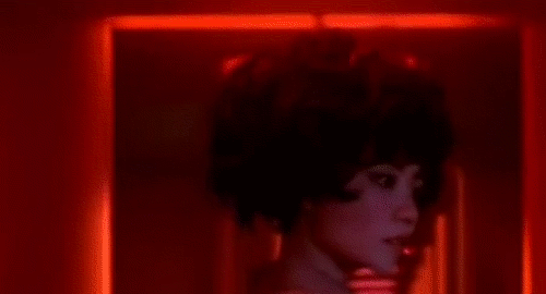 An animated gif of a scene from the film '2046' of a female android with big hair unnaturally turning her head towards the camera.