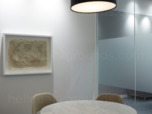 Intimate meeting room containing round grey table with green chairs and decorated with wall mounted modern art piece   Microsoft Teams background