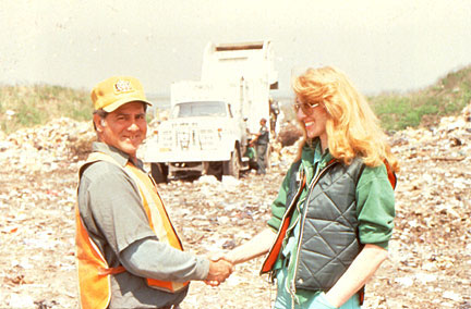 Mierle Ukeles shakes the hand of a New York City sanitation worker, against the backdrop of a landfill.