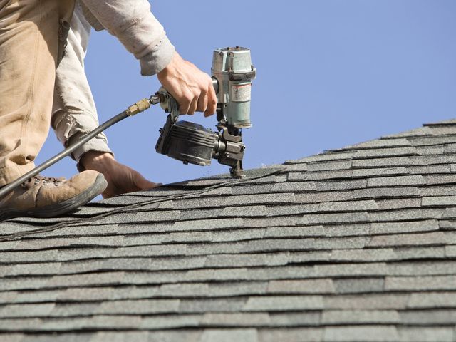 Roof worker using nail gun to install roof shingles