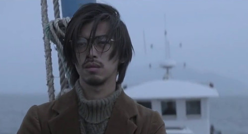 A screenshot from the Chinese movie 'The Continent' of a young man with glasses and hair in his face looking dejected on a boat.