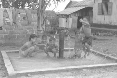 Five children playing around a standpipe spouting water in Geylang Serai.