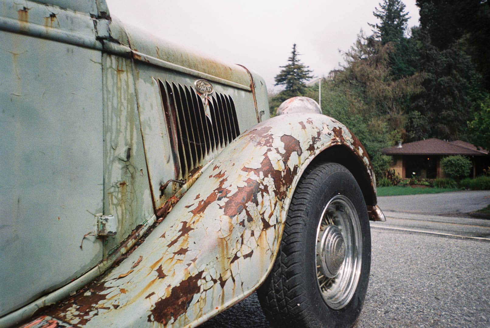 Old 1930s era Ford with weathered and pealing pale green paint in a light rain