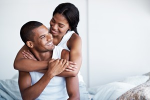 Shot of a woman hugging her husband from behind while sitting on their bed birth control method for men vasectomy