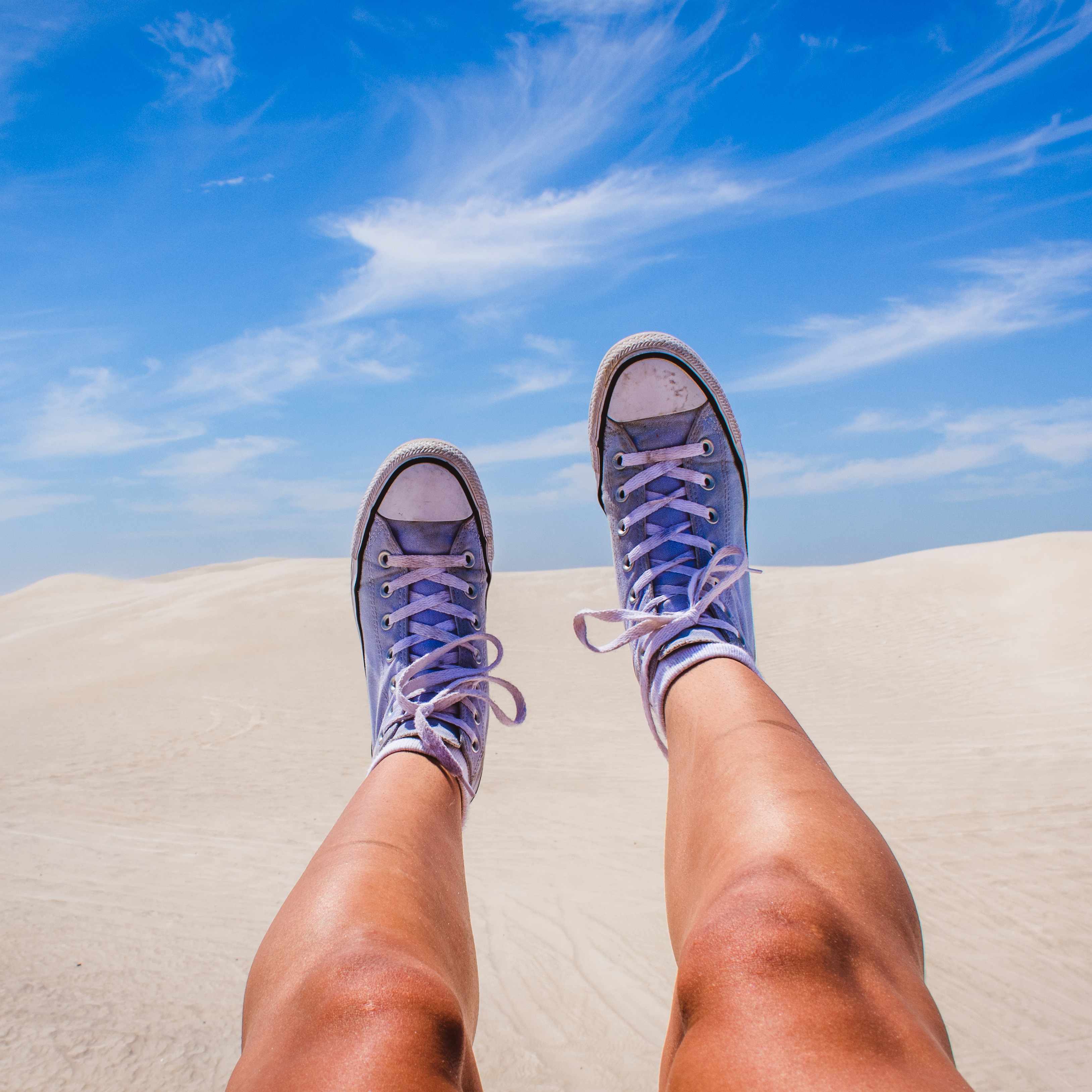 Point of view shot showing two legs in the air, with purple shoes, appearing above a desert dune.