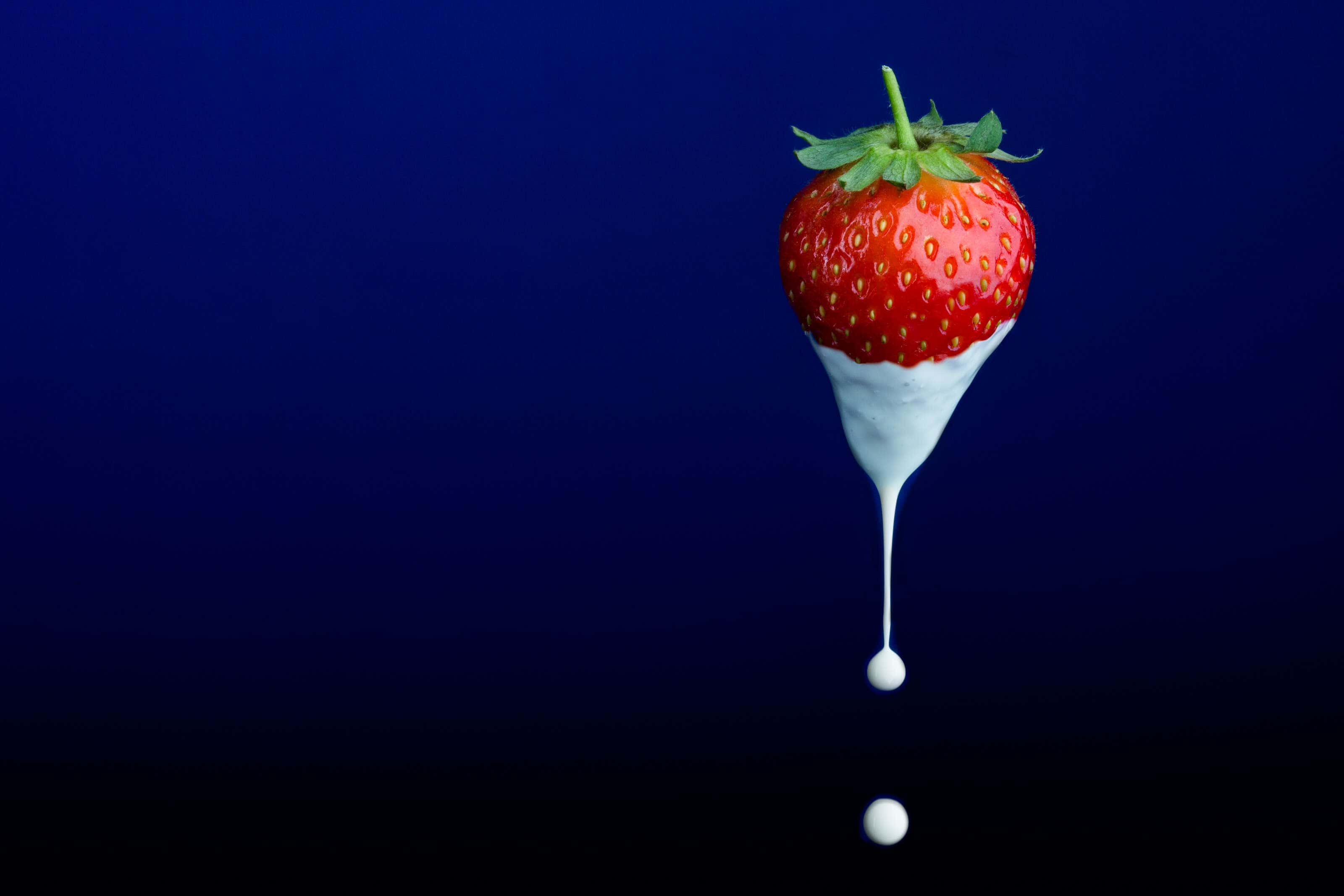 a strawberry suspended mid air with a drip of cream falling off it.with a drip of cream