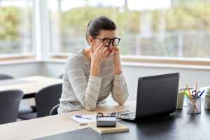 Woman rubbing her eyes, annoyed at her computer running so slow