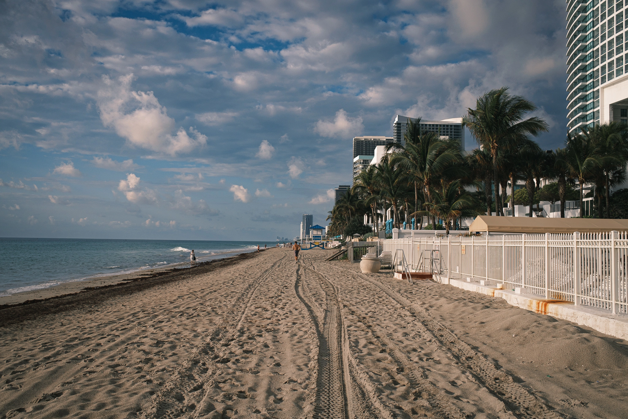 A photograph of a jogger, running down a long beach in the early morning sun.