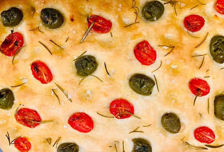 Closeup of focaccia bread studded with tomatoes, olives, and rosemary