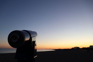 A fixed telescope pointing towards the out of focus sunset over the sea.