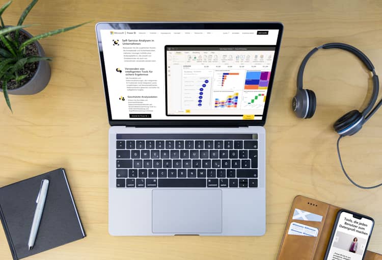 Laptop mit Power BI auf Schreibtisch mit Smartphone, Pflanze, Kopfhörern