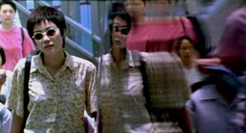 A psychedelic screenshot from the movie 'Chungking Express' of a young woman in sunglasses and short black hair. The right half of the image is a warped reflection of her on stainless steel wall.