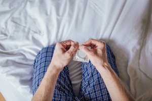 Man sitting in the bed tearing open condom packet for protection during sex contraceptive