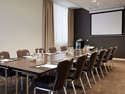 Conservative style boardroom containing large metal framed wooden table with brown fabric chairs and projector screen Microsoft Teams background